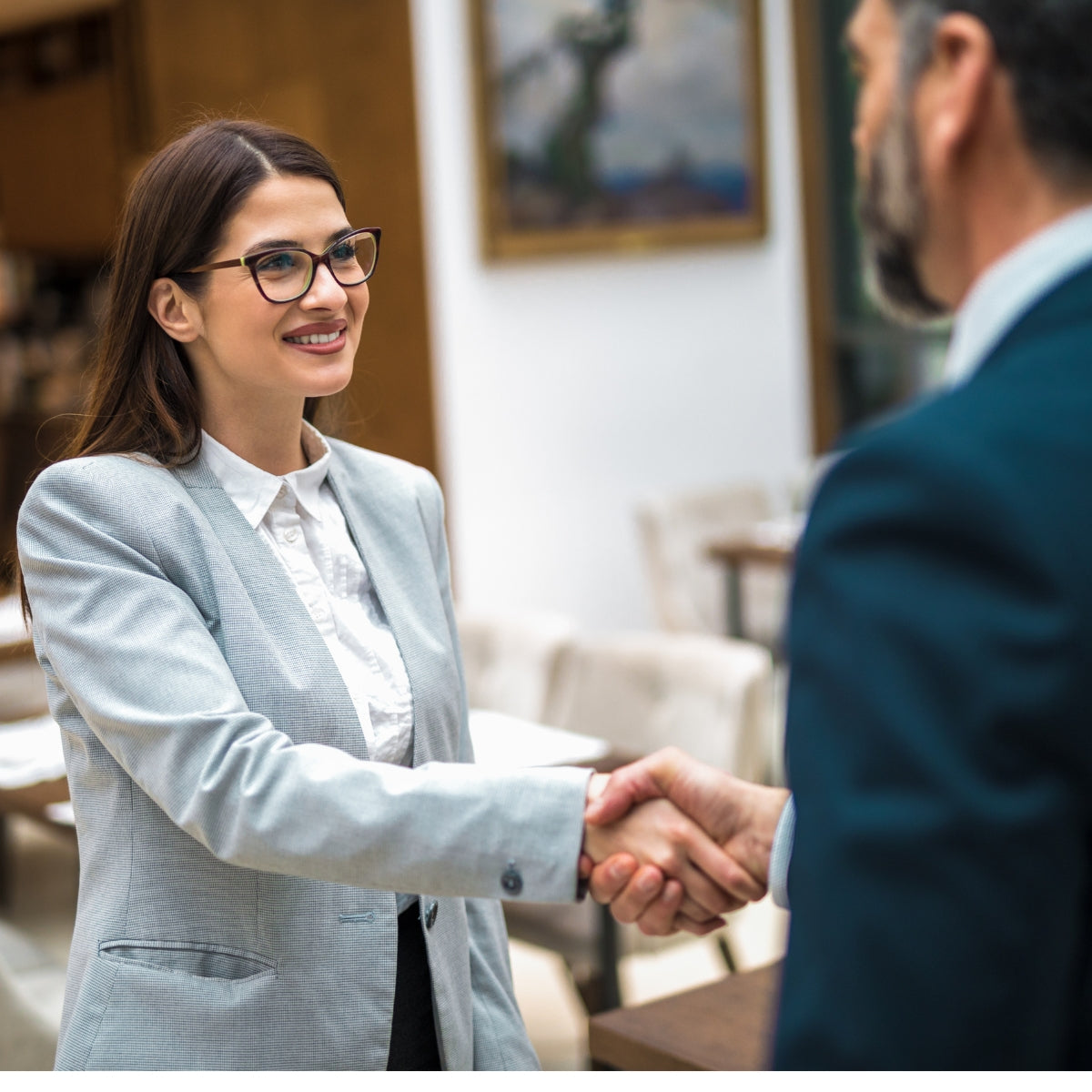 Business professionals shaking hands in a modern office or restaurant setting, symbolizing agreement or partnership.
