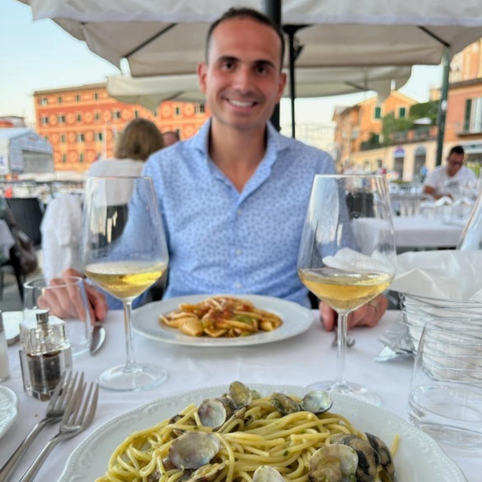 A man enjoying a dinner of seafood pasta and white wine at an outdoor restaurant with scenic views.