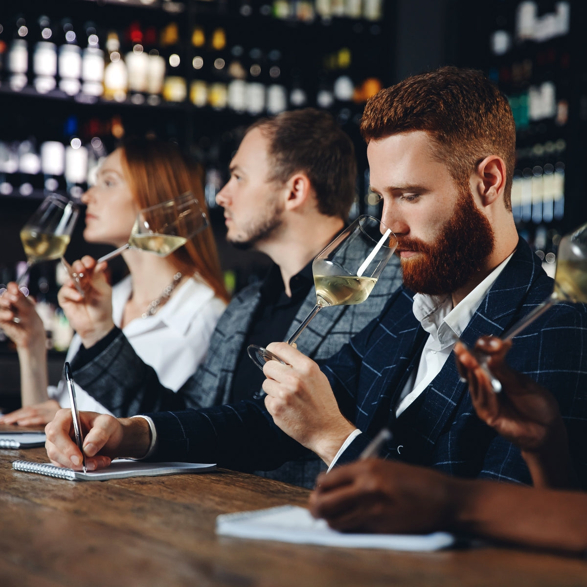 Group of sommeliers holding glasses of white wine and taking notes during a wine tasting session.