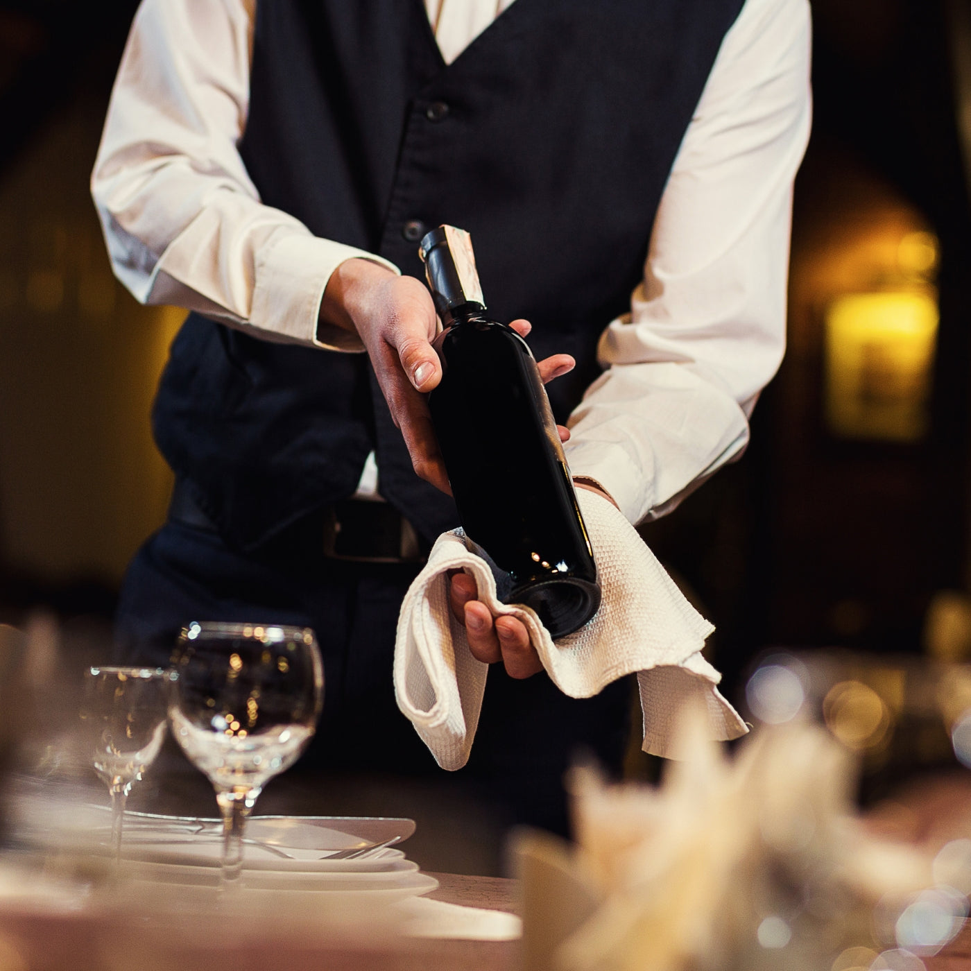 Waiter in uniform presenting a bottle of wine with a white towel in a fine dining restaurant.