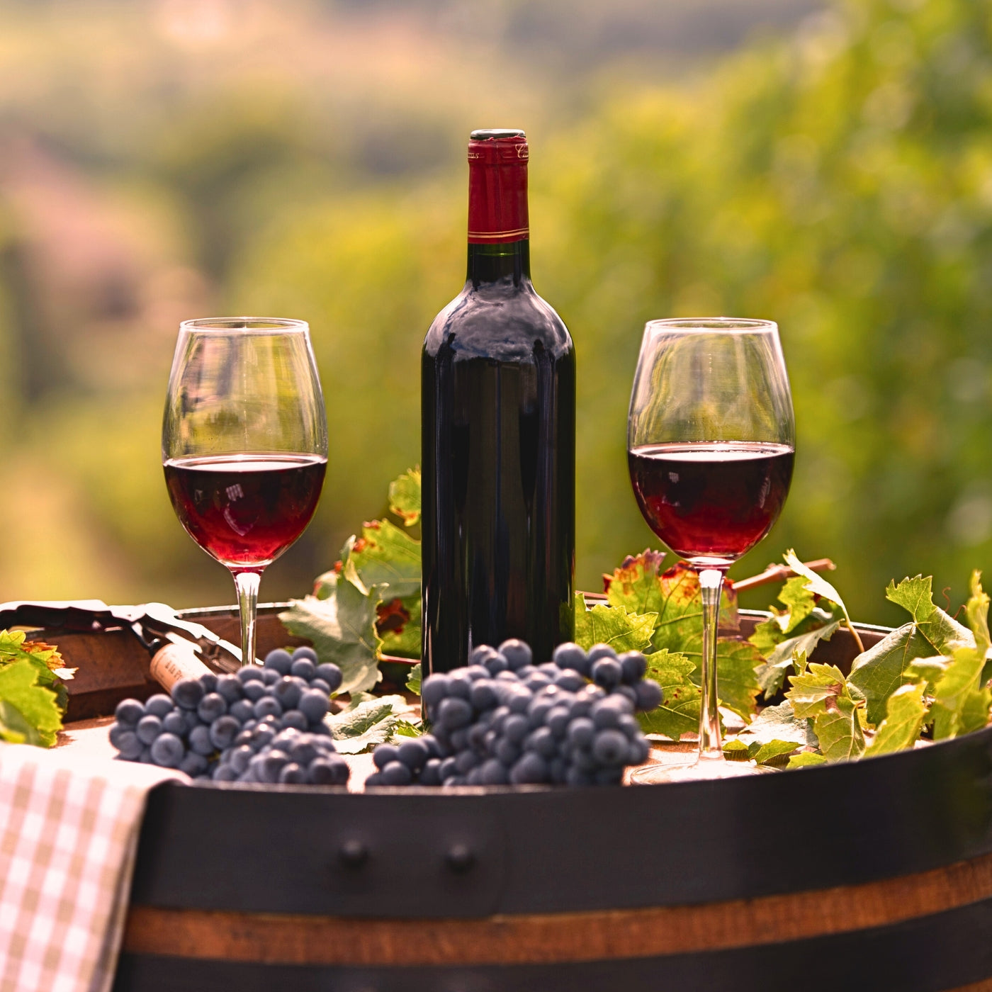 A bottle of red wine with two glasses on a wooden barrel in a lush Bordeaux vineyard, France, with grapes and vines in the background.